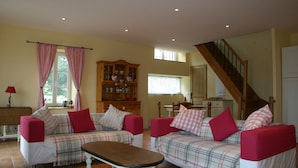 A living room with two sofas, a wooden cabinet, a dining table, and a staircase.