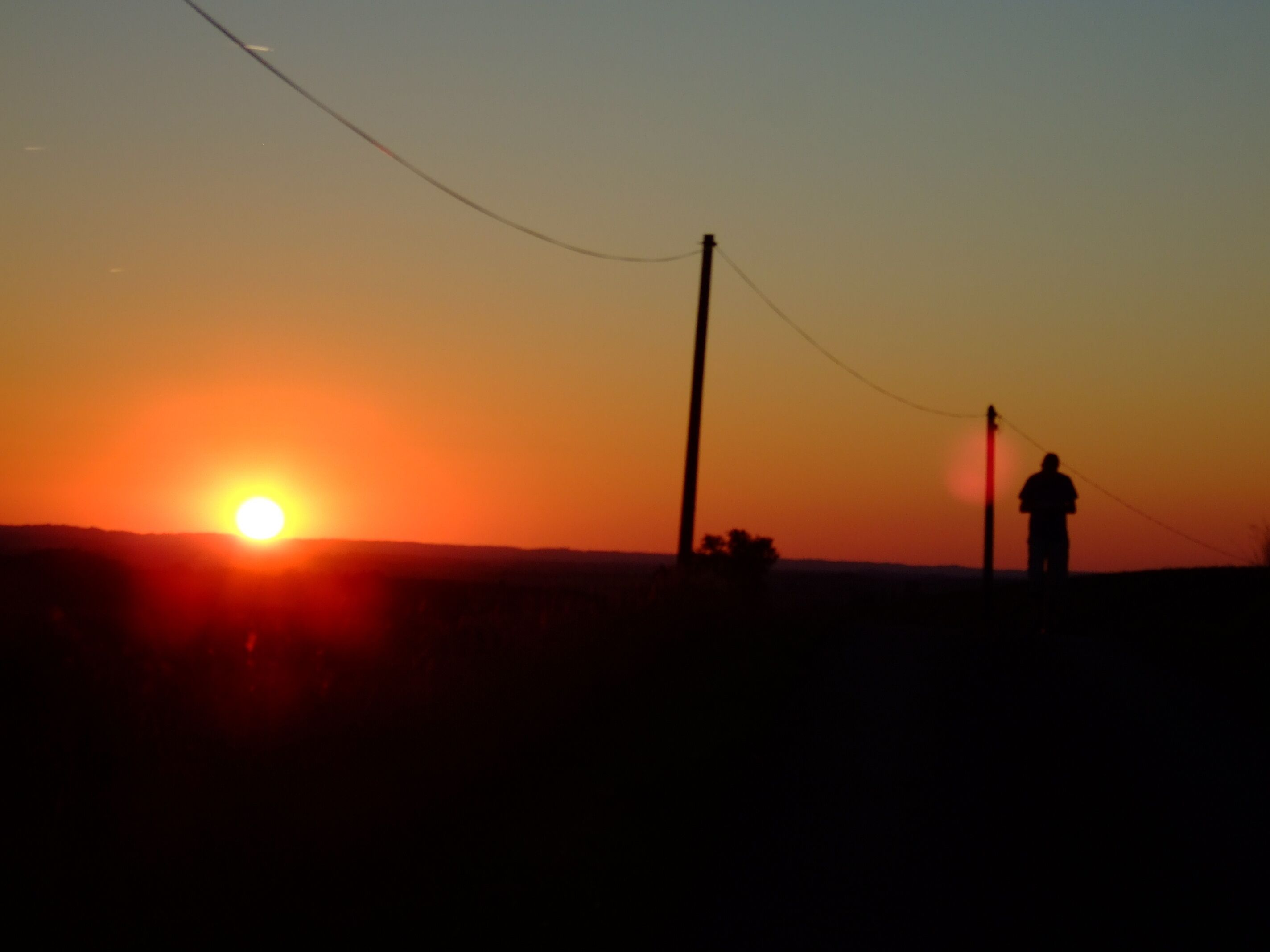 A silhouette of a person standing next to a utility pole during sunset.