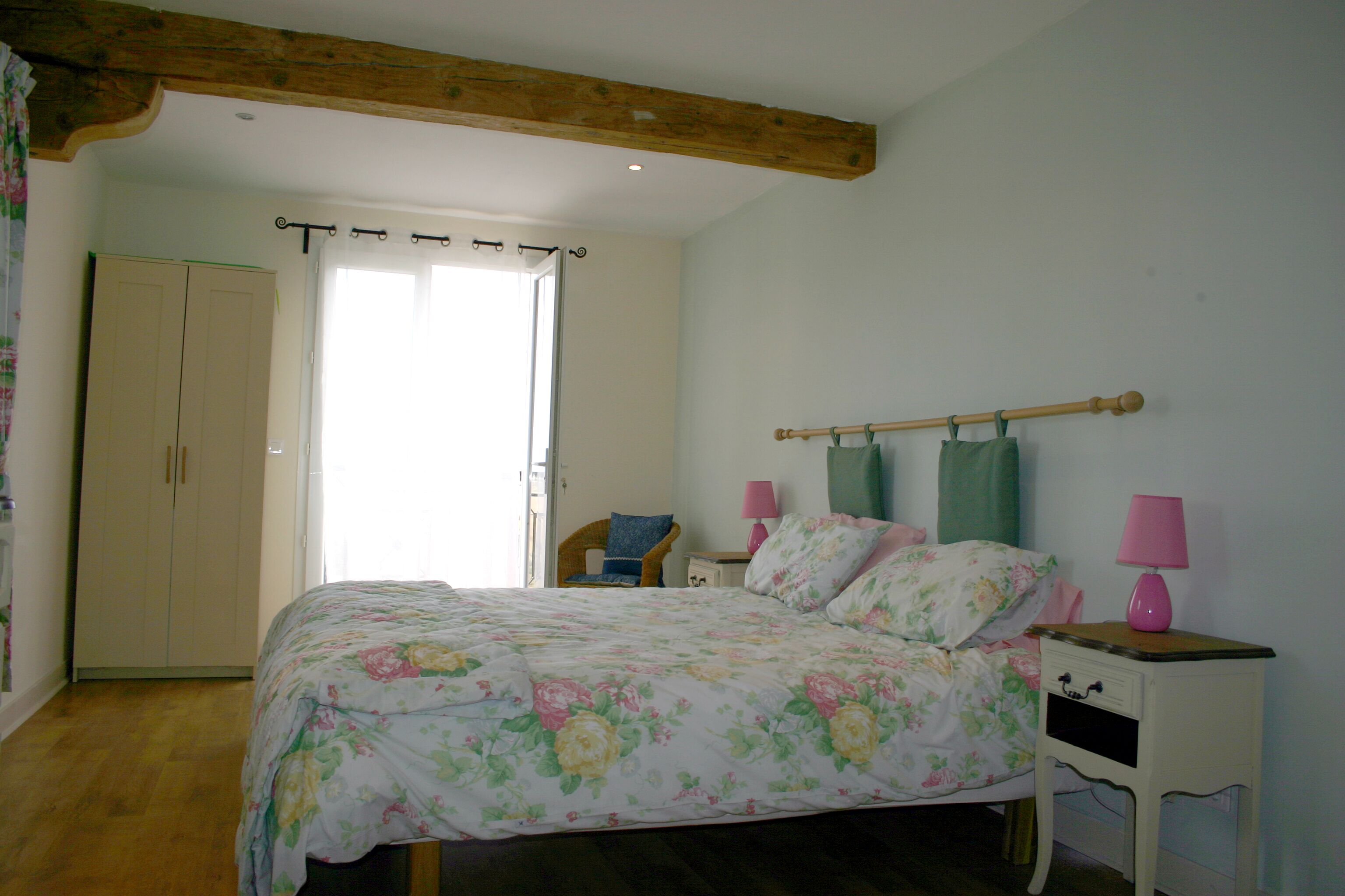 Een slaapkamer met een bed, nachtkastjes, een stoel, een kledingkast en een raam met gordijnen.