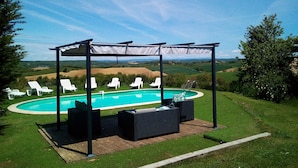 A pool area with a pergola, lounge chairs, and a view of the countryside.