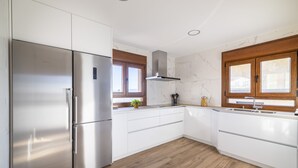 Une cuisine moderne avec des meubles blancs, un réfrigérateur en acier inoxydable, un plancher en bois et une fenêtre offrant une belle vue.