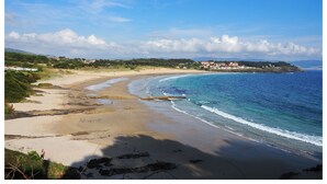 Un paysage côtier avec une plage de sable, un ciel bleu dégagé et une vue lointaine sur des bâtiments situés sur une colline.