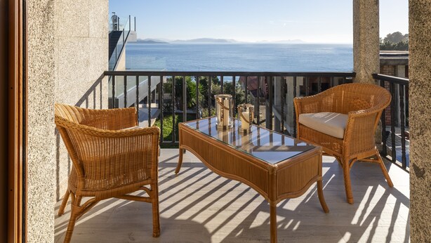 Un balcon agrémenté de meubles en osier, d’une table en verre et offrant une vue sur la mer.