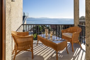 Een balkon met rieten meubels, een glazen tafel en uitzicht op zee.