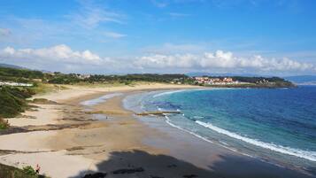 A coastal landscape with a sandy beach, a clear blue sky, and a distant view of buildings on a hill.