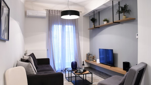 A modern living room with a sofa, armchair, coffee table, TV, and shelves with plants. - Alpinia Deluxe Apt Must (Thessaloniki)