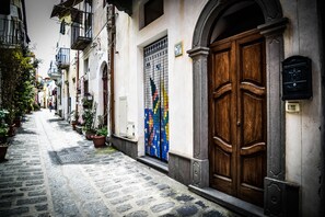 Una estrecha calle adoquinada flanqueada por edificios, una puerta de madera grande y un portón colorido.
