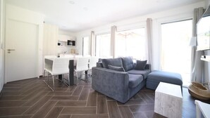 A modern living room with a grey sofa, a white coffee table, and a dining area with white chairs. - Villa 3 by Avecoeur (Saint-Augustin)