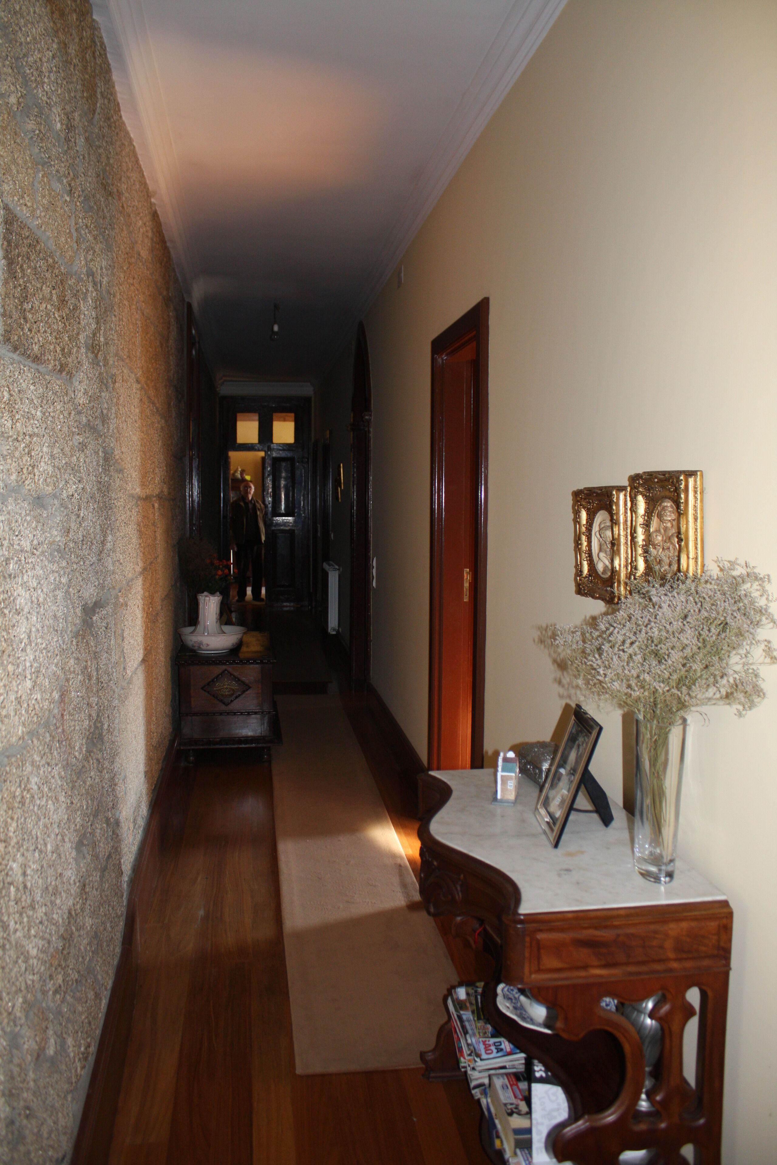 Un corridoio con pavimento in legno, parete in pietra, una porta in legno e un tavolo con un vaso di fiori.