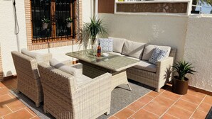 Un patio con mobiliario de mimbre, una mesa de vidrio y plantas en macetas.