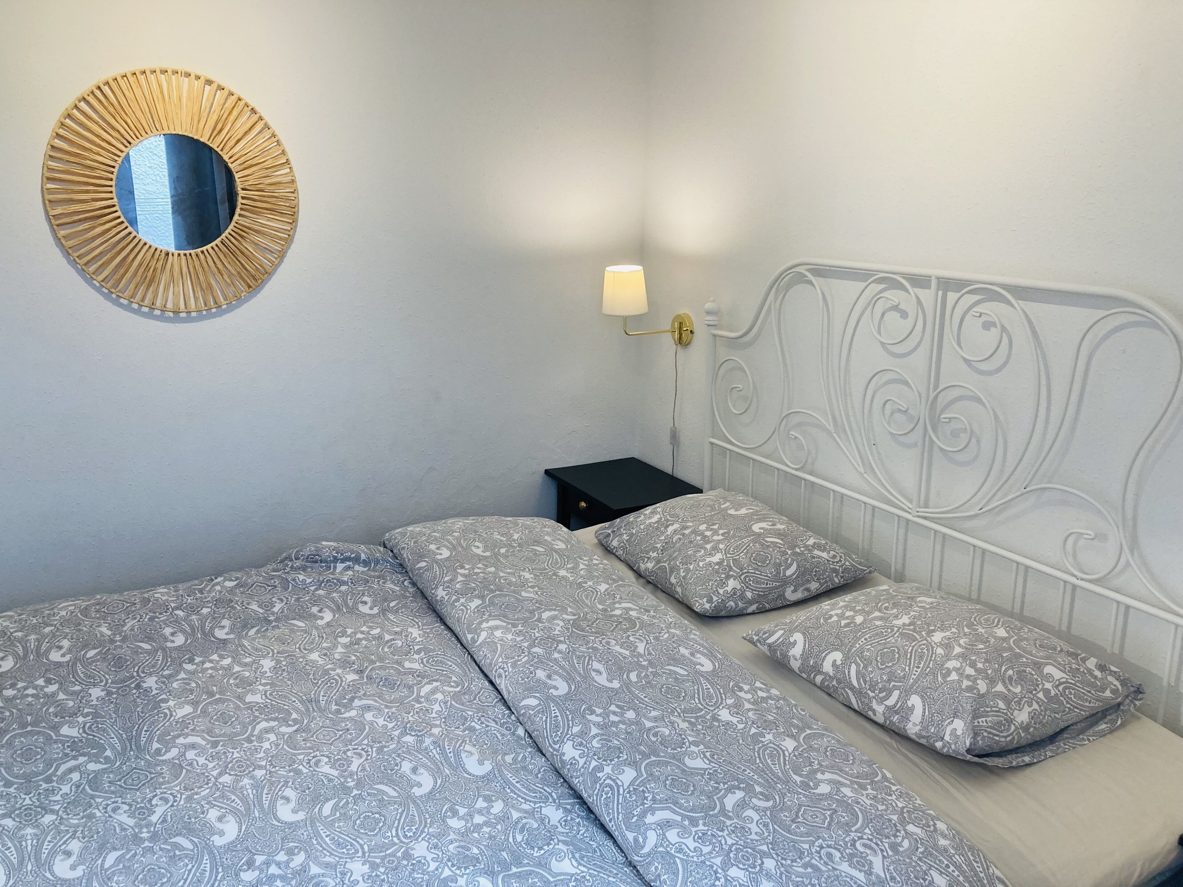 Et soveværelse med en seng, et natbord, en lampe og et spejl på væggen.