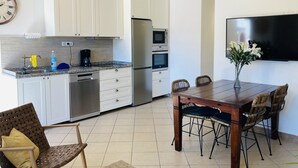 Una cocina moderna con armarios blancos, electrodomésticos de acero inoxidable y un comedor con sillas de mimbre y una mesa de madera.