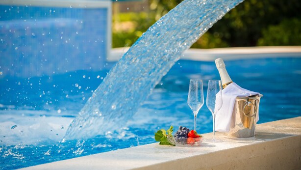 Ein Pool mit Wasserfall, eine Flasche Champagner, zwei Gläser und eine Obstschale.