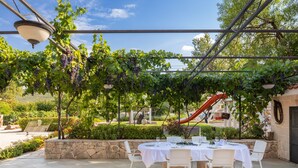 Ein Essbereich im Freien mit einem Tisch für vier Personen, umgeben von Steinmauern und einer Pergola mit Weinstöcken.