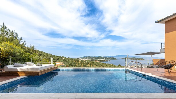 A swimming pool with a view of the sea and hills, a lounge area with a sofa and cushions, and a chair. - IO.DELUXE 2ΒR, 2 BTHR.VILLA WITH PRIVATE POOL  AND STUNNING SEA VIEWS  (SKIATHOS)