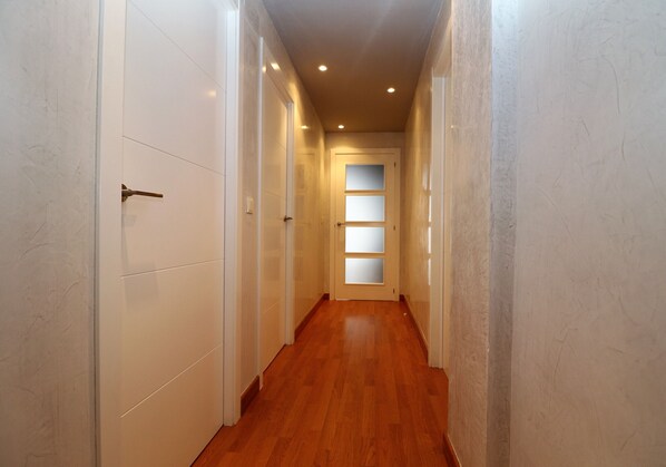 Un couloir étroit aux murs blancs et au plancher en bois, qui mène à une porte dotée de panneaux en verre dépoli.
