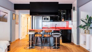 A modern kitchen with a red countertop, black cabinets, and a stainless steel sink. There are three bar stools with leather seats and a small round table. The floor is wooden, and there is a plant on the right side. - Las Palmas 2-10 Apartment Old Town (Benidorm)