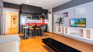 A modern living room with a sofa, a coffee table, a TV, and a kitchen area with a red countertop and stools. - Las Palmas 2-10 Apartment Old Town (Benidorm)