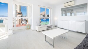 A modern living room with a large window, white furniture, and a view of buildings and water. - Veracruz 18-A (Benidorm)