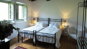 A double bed with white linens, two bedside tables with lamps, a wicker chair, a wooden floor, and a window with shutters. - Relaxing and stilish home only 30 minutes from Florence in Chianti Region (San Polo in Chianti)