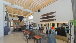 A spacious kitchen with a bar area, wooden ceiling beams, and a large window providing natural light. - The One @ Pezula  (Knysna)