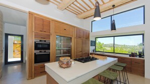 A modern kitchen with wooden cabinets, a large island, and a view of the countryside. - The One @ Pezula  (Knysna)