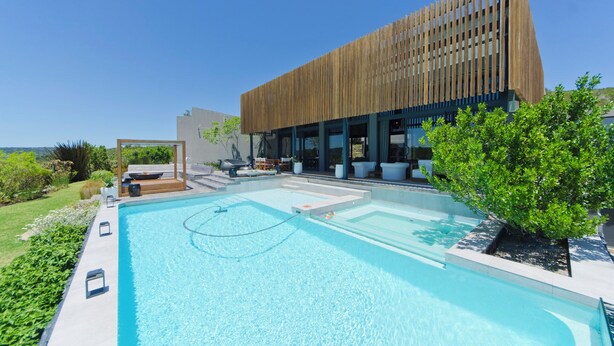 A modern building with a pool area, including a large pool, a wooden deck, and outdoor seating. - The One @ Pezula  (Knysna)
