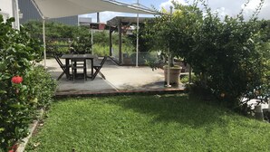 Een terras met een tafel en stoelen, omgeven door groen en een grote parasol.