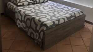 Een eenpersoonsbed met een bedsprei met patroon, een houten hoofdbord, een witte hemel en een raam met gordijnen.