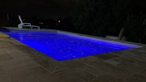 Een rechthoekig zwembad met een blauw verlichte rand, omgeven door een stenen terras.