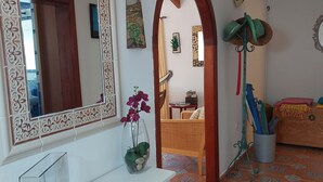 A room with a white console table, a large mirror, a decorative archway, a small table with a plant, and a bed with a red blanket.