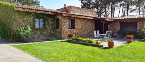 A stone house with a tiled roof, a patio with outdoor furniture, and a well-maintained lawn.