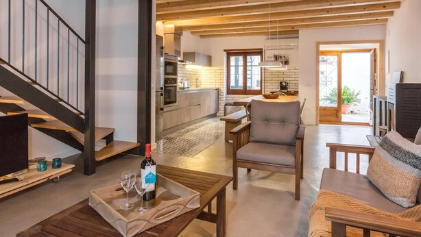 A spacious living area with a wooden staircase, a dining table with chairs, and a kitchen in the background.