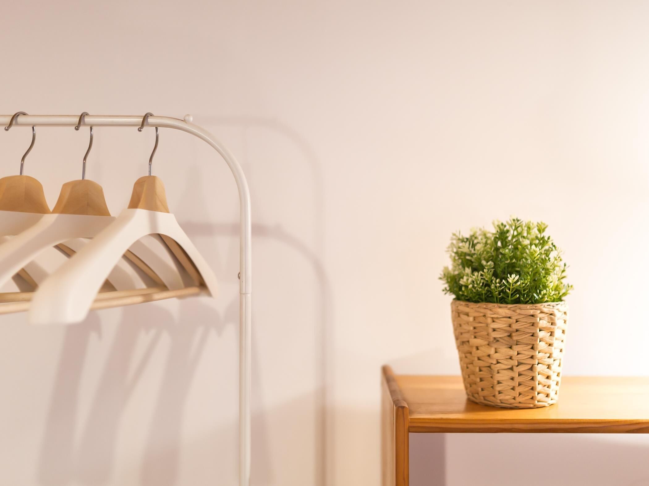 A metal coat rack with wooden hangers and a woven basket with a plant on a wooden table.