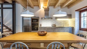 A modern kitchen with a wooden dining table, two pendant lights, and a built-in oven.