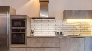 A modern kitchen with stainless steel appliances, a white tiled backsplash, and a built-in oven.