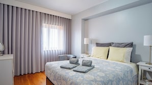 Una camera da letto con un letto, due comodini, un tavolo da notte, una lampada, uno specchio e una finestra con tende.