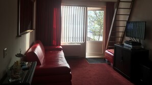 Una habitación con un sofá rojo, un televisor sobre un mueble, una ventana con cortinas y una puerta que da al exterior.