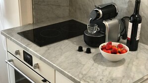 A kitchen with a black coffee maker, a bowl of strawberries, and a wine bottle.