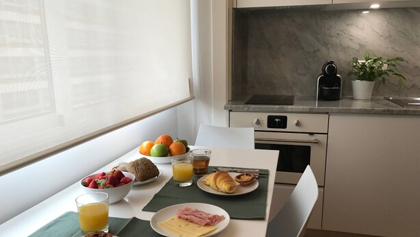 A breakfast table with croissants, ham, cheese, strawberries, and oranges.