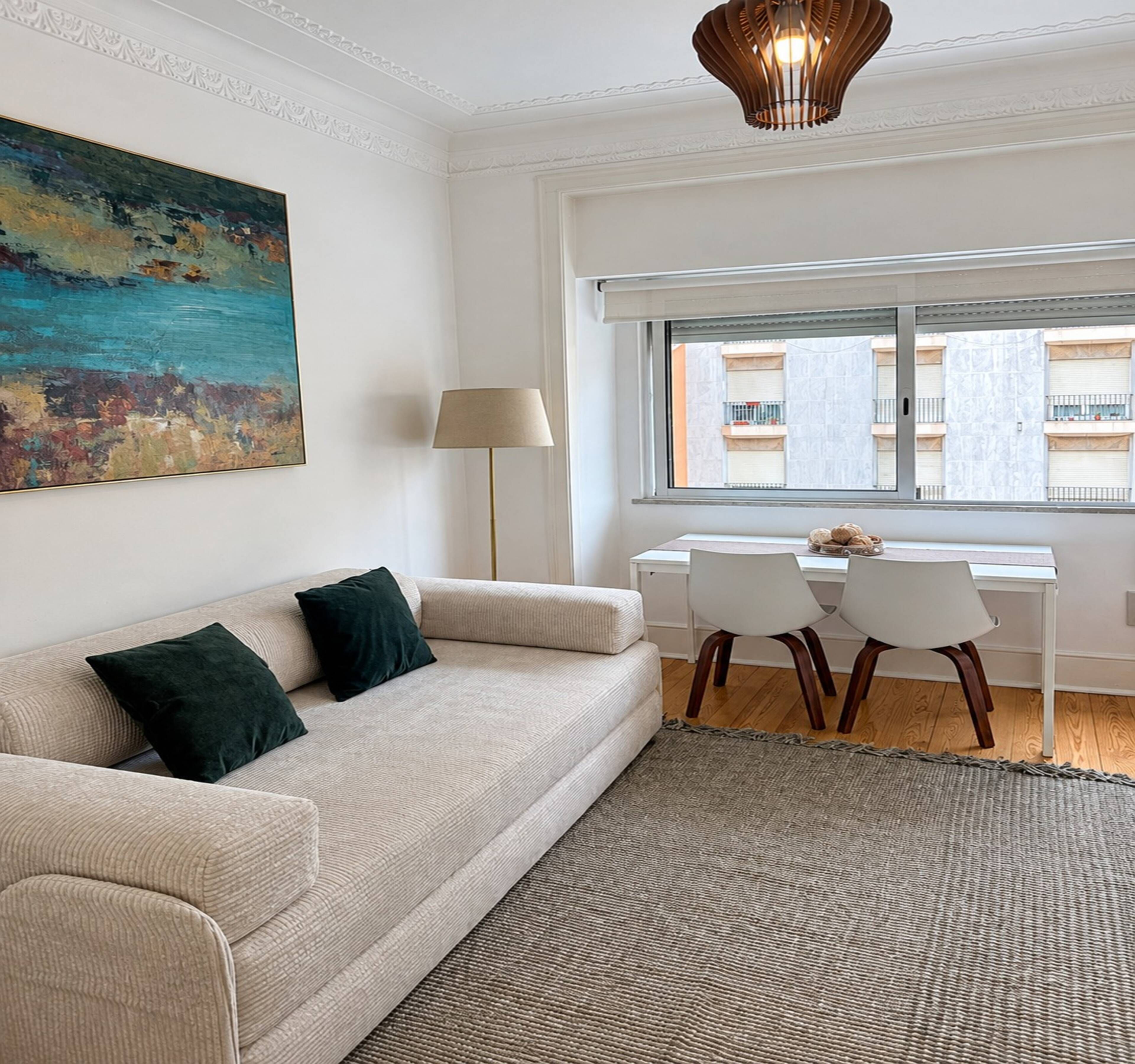 Una sala de estar moderna con un sofá, una mesa de comedor con sillas, una lámpara y un cuadro en la pared.