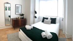 A neatly arranged bedroom with a bed, a dresser, a mirror, and a window.