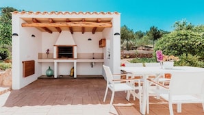 Eine Außenpatio mit integriertem Grill, weißen Möbeln und Blick auf die umliegende Landschaft.