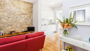 A living room with a red sofa, a stone wall, a kitchen in the background, and a vase with flowers on a white console table.