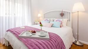 A neatly made bed with a tray of breakfast items, a bedside lamp, and a decorative heart on the headboard.