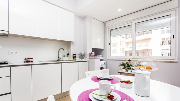 A modern kitchen with white cabinets, a dining table with pink placemats, and a coffee maker.