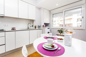 A modern kitchen with white cabinets, a dining table with pink placemats, and a coffee maker.