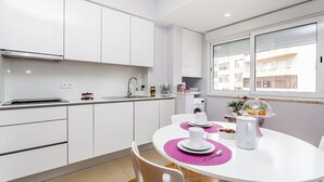 A modern kitchen with white cabinets, a dining table with pink placemats, and a window with a view of buildings.