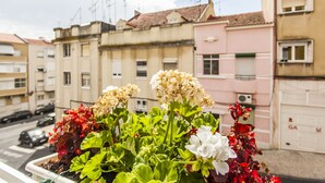 A balcony with potted plants and a view of a residential street with buildings.