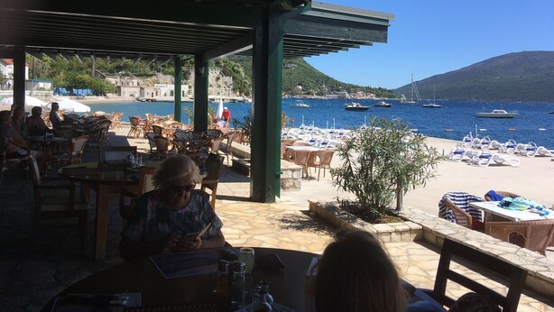 A seaside restaurant with outdoor seating overlooking a beach and the sea.